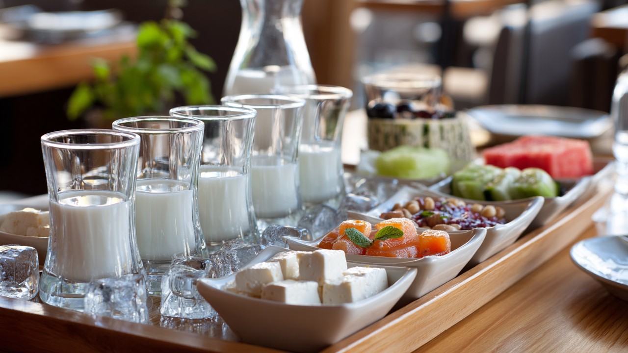 Rakı servisi ve çeşitli mezelerle güzel düzenlenmiş ahşap masada, buzlu rakı bardakları ve renkli meze tabaklarıyla sıcak atmosfer.